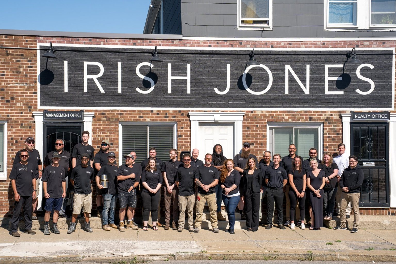 The Irish Jones team in black polos outside the brick Bailey Avenue office in Buffalo